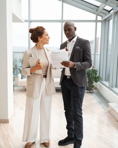 Woman in cream suit and man in gray blazer reviewing documents in bright office